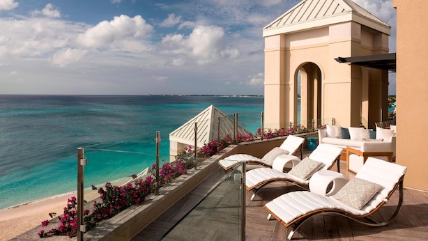 A balcony with lounge chairs overlooking a beach and ocean.