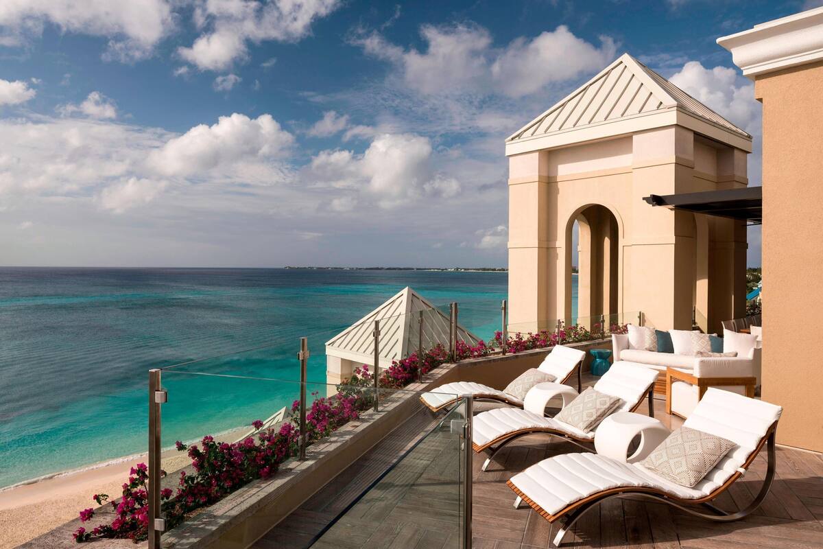 A balcony with lounge chairs overlooking a beach and ocean.