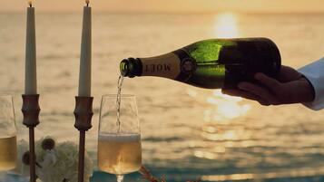 Botella de champán siendo servida en una copa, con una vela y flores sobre una mesa frente al mar.