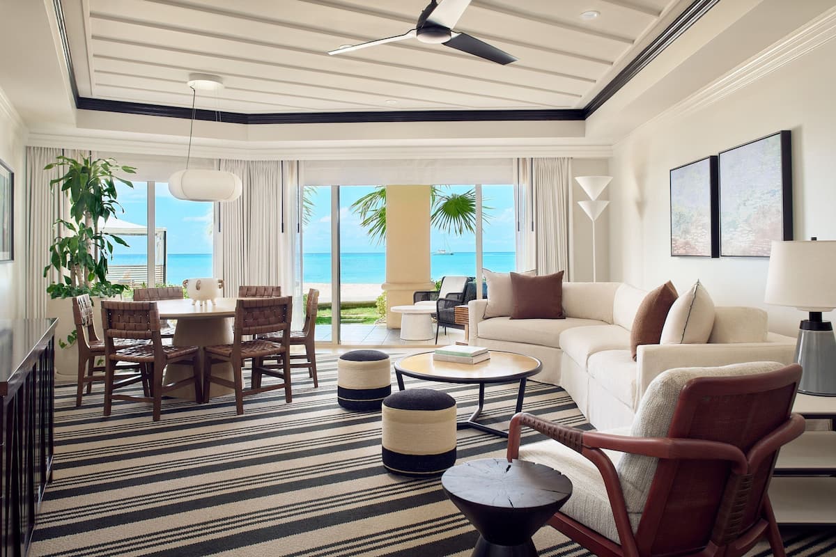 A spacious living room with a large window overlooking the ocean, a dining area with wooden chairs, a sofa, and a coffee table.