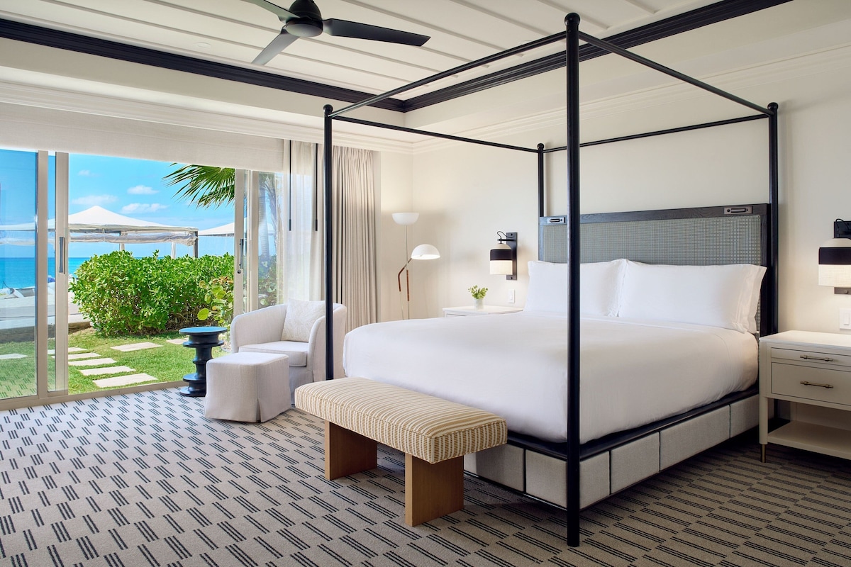 A four-poster bed with a white mattress and pillows, a bedside table with a lamp, and a bench.