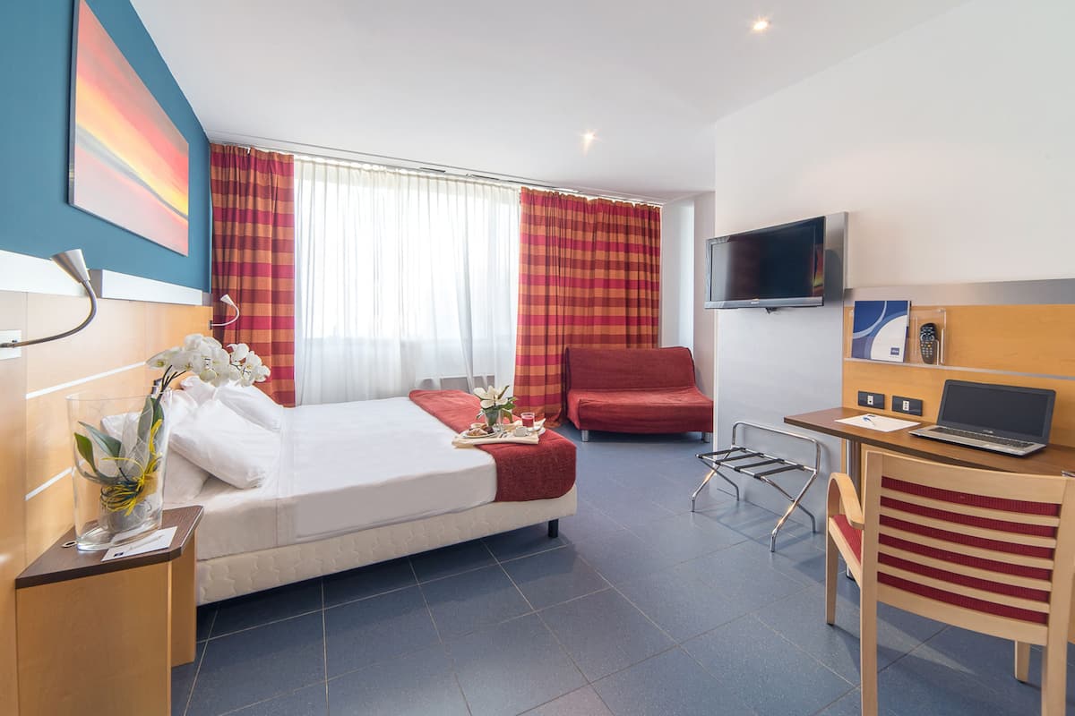 Una habitación de hotel con una cama, un escritorio con una computadora portátil, un televisor y una silla.