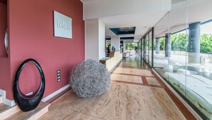 A modern hotel lobby with a reception desk, a large glass window, and a unique spherical sculpture on the floor. - Sotel Nomentana (Rome)