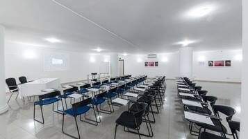 A conference room with rows of chairs, tables, and a projector screen.