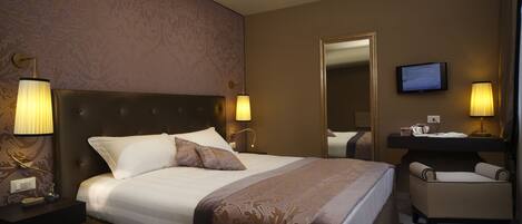 A hotel room with a large bed, two bedside lamps, a television, a mirror, and a small chair.