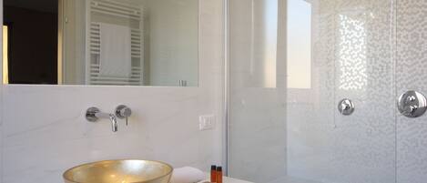 Un baño moderno con un lavabo dorado grande, una encimera blanca, una ducha con mampara de vidrio y un espejo grande.