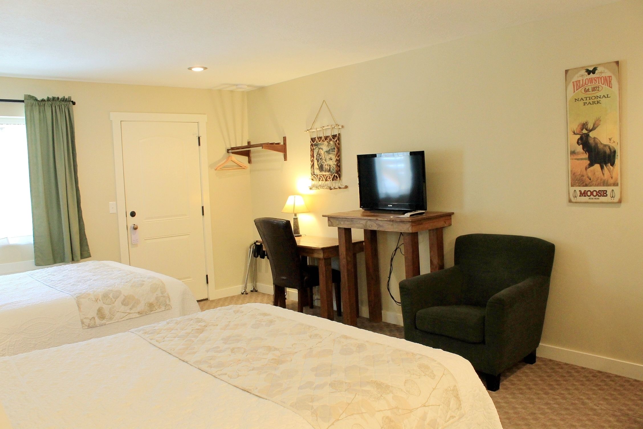 Une chambre d’hôtel avec deux lits, un bureau avec une télévision, une chaise, une lampe et une affiche du parc national de Yellowstone accrochée au mur.