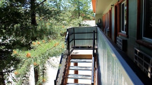 A wooden staircase leading to a balcony with a metal railing, surrounded by trees and a building with windows and a door. - Moose Creek Inn (West Yellowstone)