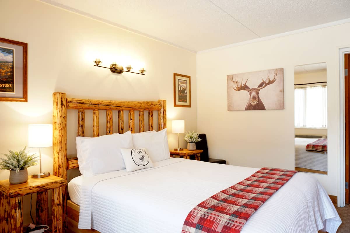 A bedroom with a wooden headboard, white bedding, a red plaid throw, and wall-mounted lighting.