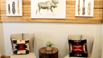 A room with two armchairs, each with a unique patterned pillow, a small round wooden table with a plant, and three framed animal prints on the wall.