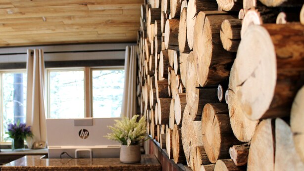 A kitchen with a wooden log wall, a countertop, and a window with curtains. - Moose Creek Inn (West Yellowstone)