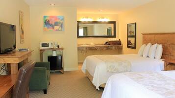 Quarto de hotel com duas camas, uma escrivaninha com televisão, micro-ondas, cafeteira e um espelho grande sobre a toucador.