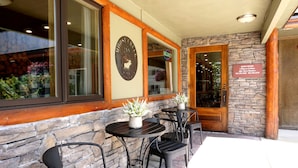 An outdoor seating area with stone walls and wooden accents, featuring tables and chairs, a 'House Inn' sign, and a 'Vacancy' sign. - Moose Creek Inn (West Yellowstone)