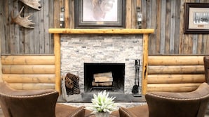 A log cabin interior with a stone fireplace, leather chairs, and antler decorations. - Moose Creek Inn (West Yellowstone)