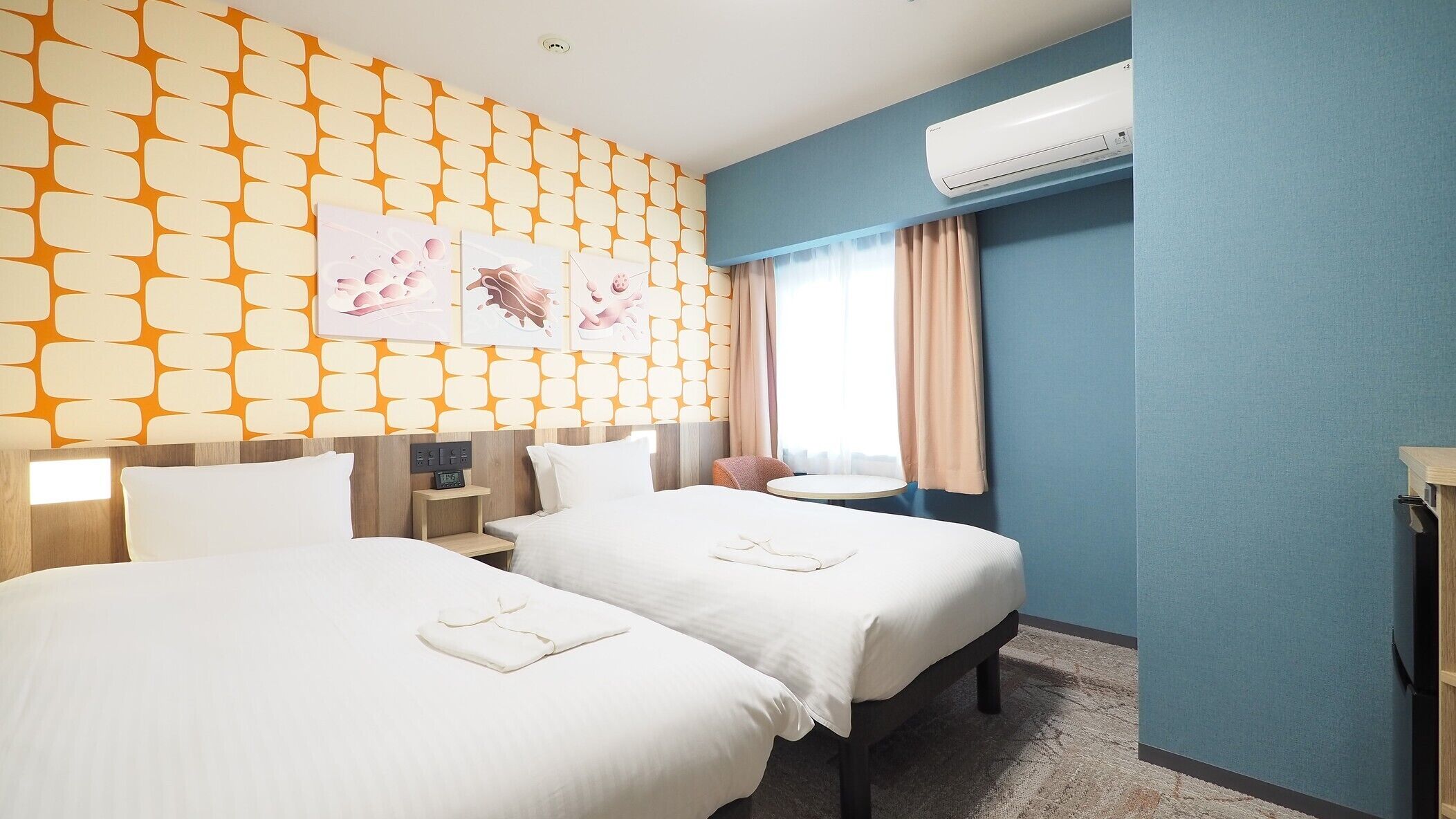 A hotel room with two beds, a nightstand, a desk, an air conditioner, and a window with curtains.
