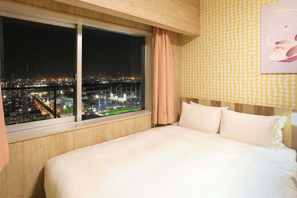 A hotel room with a large bed, a window with a city view, and a patterned wall.