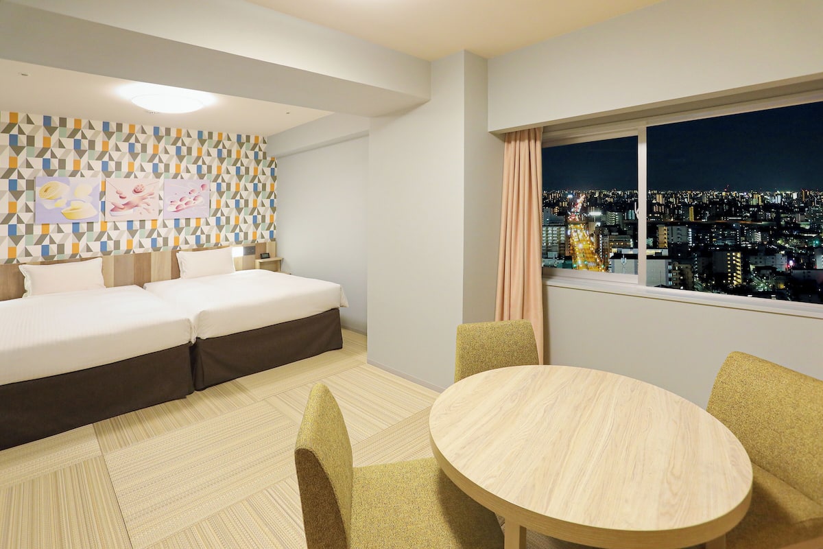 A hotel room with a bed, a dining table, and a city view.