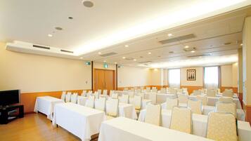 A conference room with rows of tables and chairs, a television, and a wooden floor.
