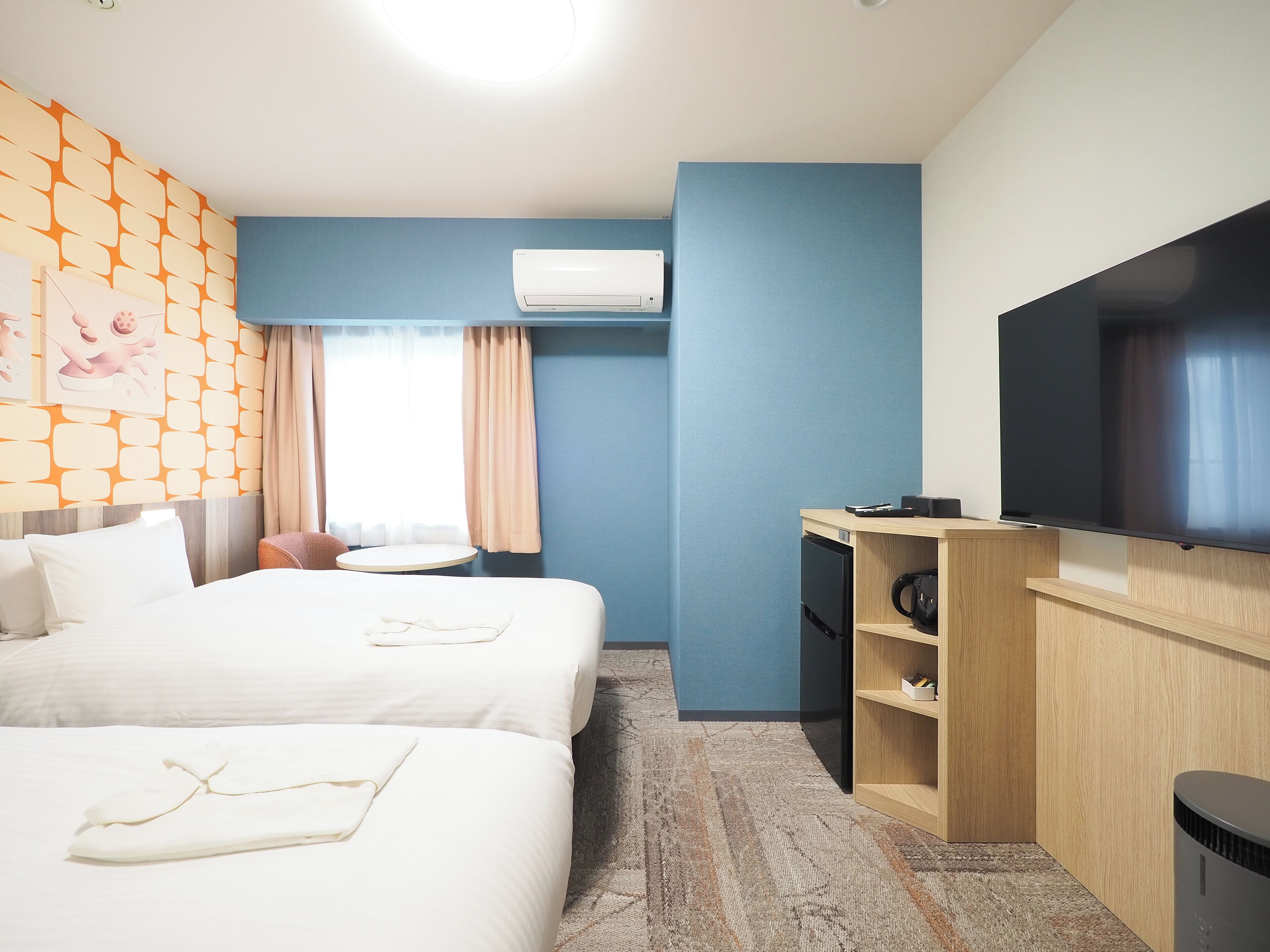Habitación de hotel con dos camas, un escritorio, un televisor de pantalla plana, una cafetera y un aire acondicionado instalado en la pared.