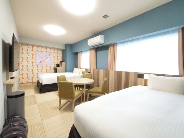 Habitación de hotel con dos camas, un escritorio, sillas, un televisor y un equipo de aire acondicionado.