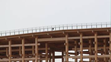 A large, multi-level wooden structure with a metal fence on top, likely a construction site.