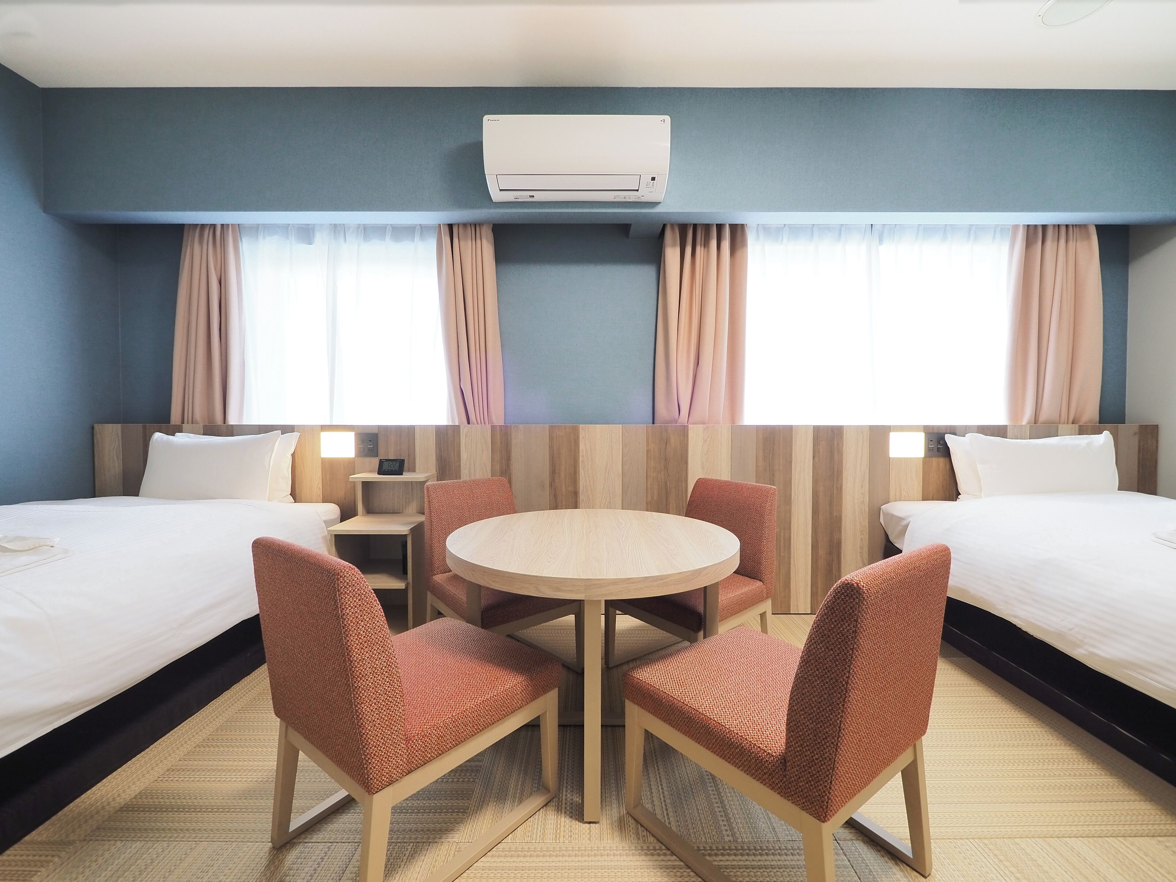 Une chambre d’hôtel avec deux lits, une table ronde et quatre chaises.