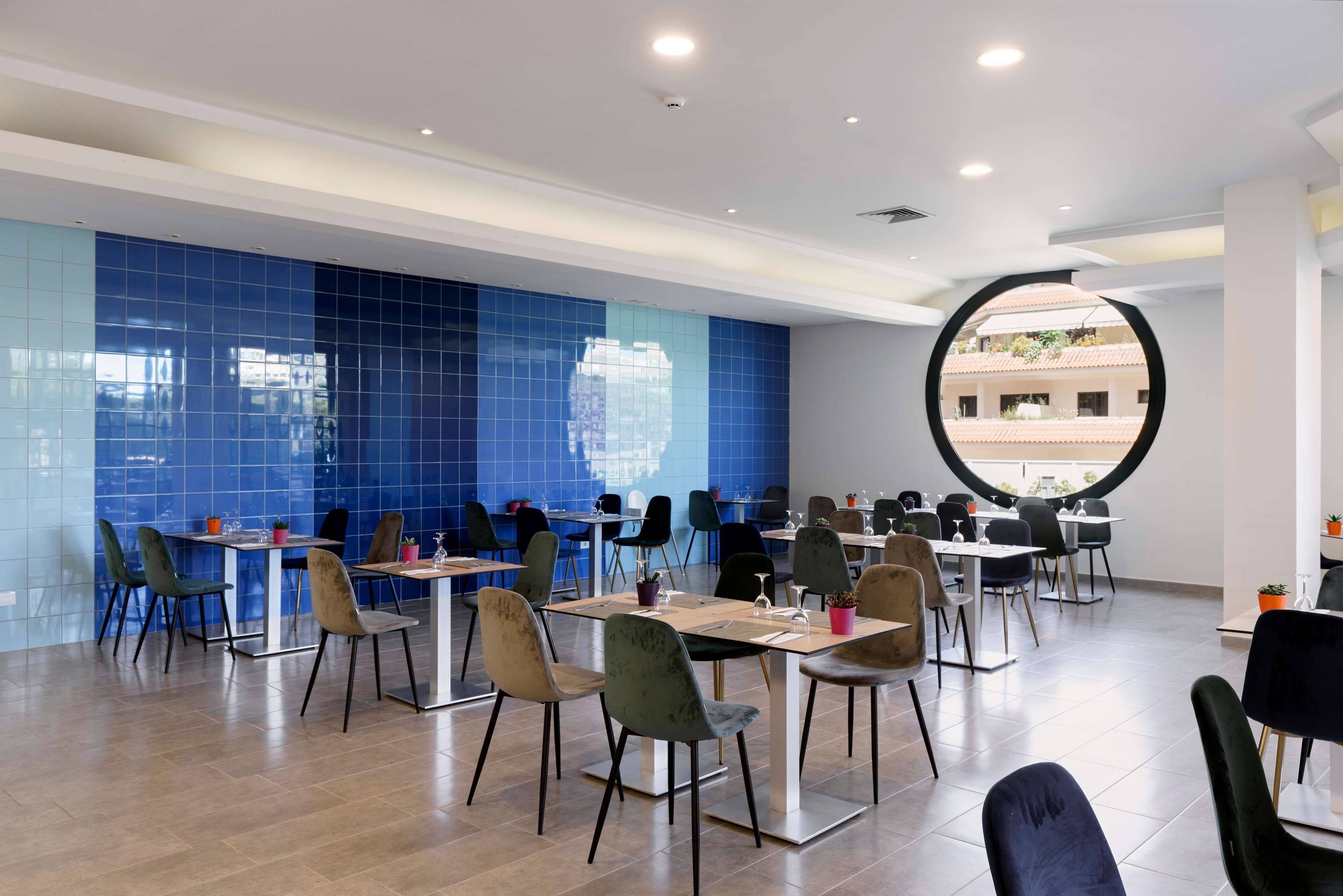Un espace de restauration moderne avec des murs recouverts de carreaux bleus, des tables rondes et des chaises contemporaines.