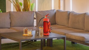 Un'accogliente area salotto esterna con una pergola in legno, un divano e un tavolo con bevande e un contenitore rosso.
