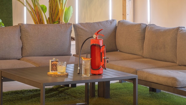 Un espacio exterior acogedor con un porche de madera, un sofá y una mesa con bebidas y un recipiente rojo.