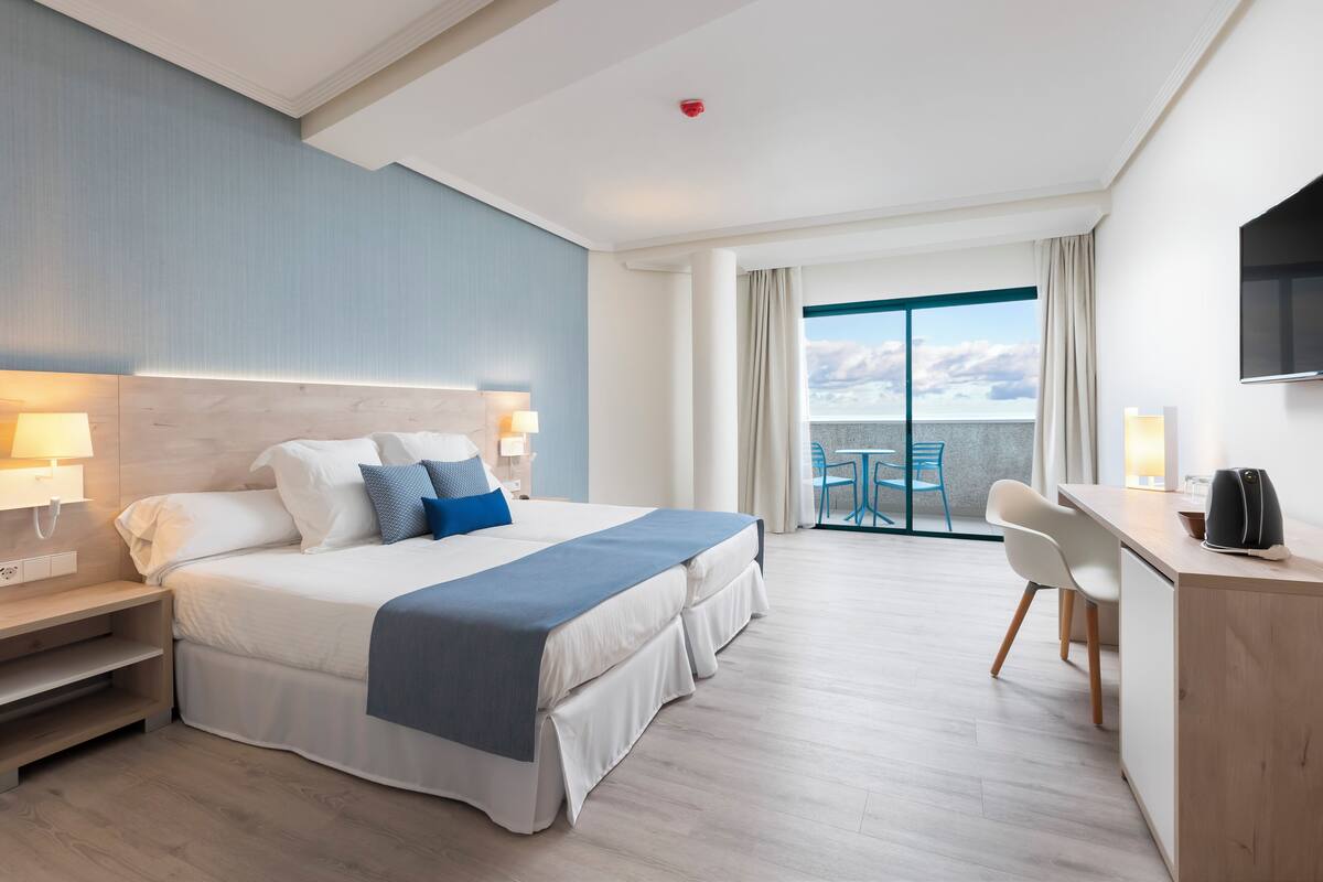 A hotel room with a bed, bedside tables, a desk, and a chair.