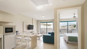 Una habitación de hotel moderna con kitchenette, zona de comedor, balcón con vistas y dormitorio independiente.