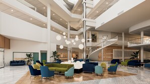 Un'ampia hall con un'area salotto centrale, una scala e un soffitto alto con luci moderne.