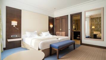 A hotel room with a bed, bedside tables, a bench, a round table, and a mirror.