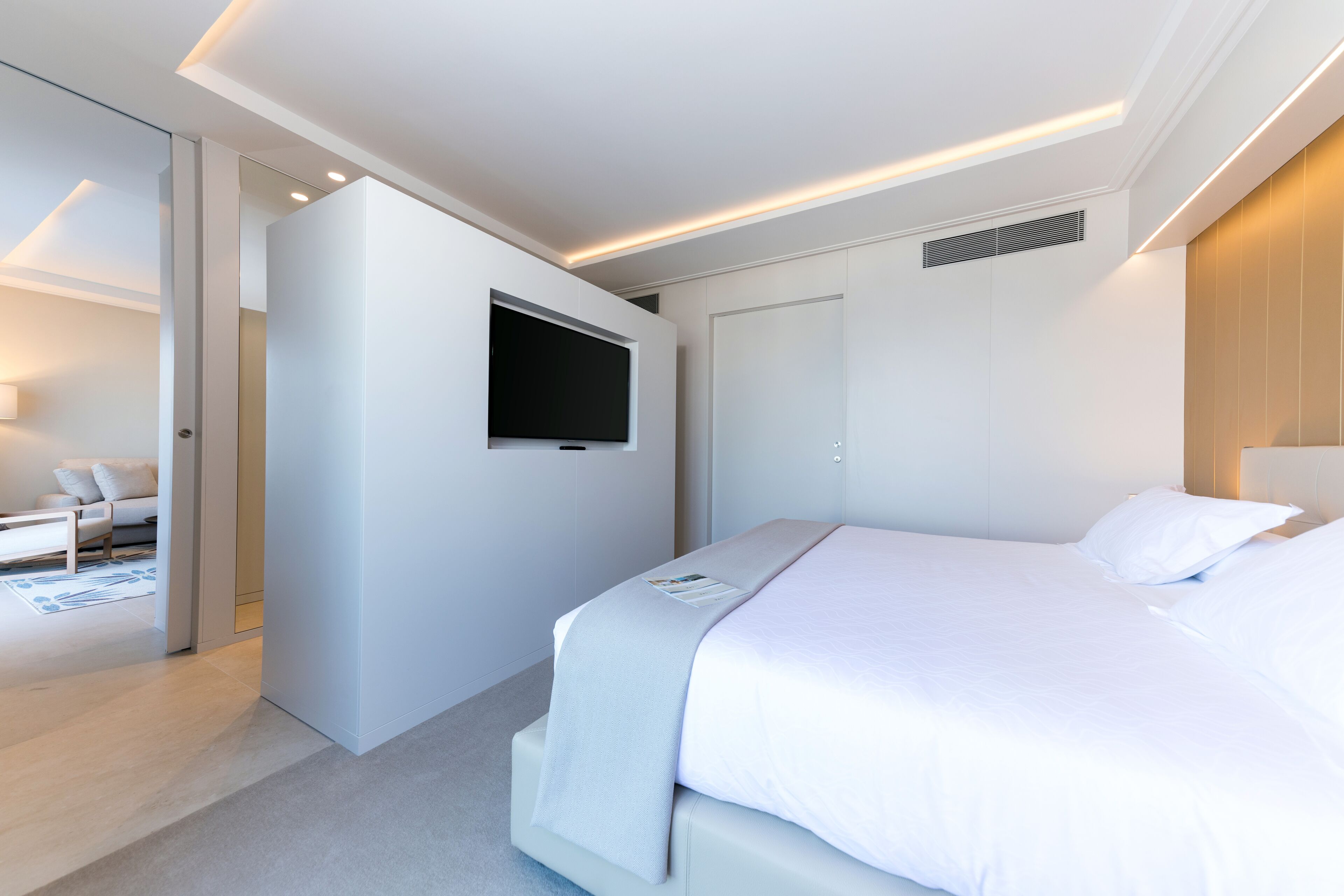 A modern hotel room with a large bed, a flat-screen TV mounted on the wall, and a separate seating area with a sofa and coffee table.