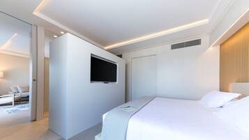 A modern hotel room with a large bed, a flat-screen TV mounted on the wall, and a separate seating area with a sofa and coffee table.