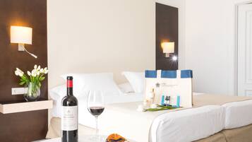Habitación de hotel con una cama, una botella de vino, una copa de vino, un jarrón con flores y un neceser de artículos de aseo.
