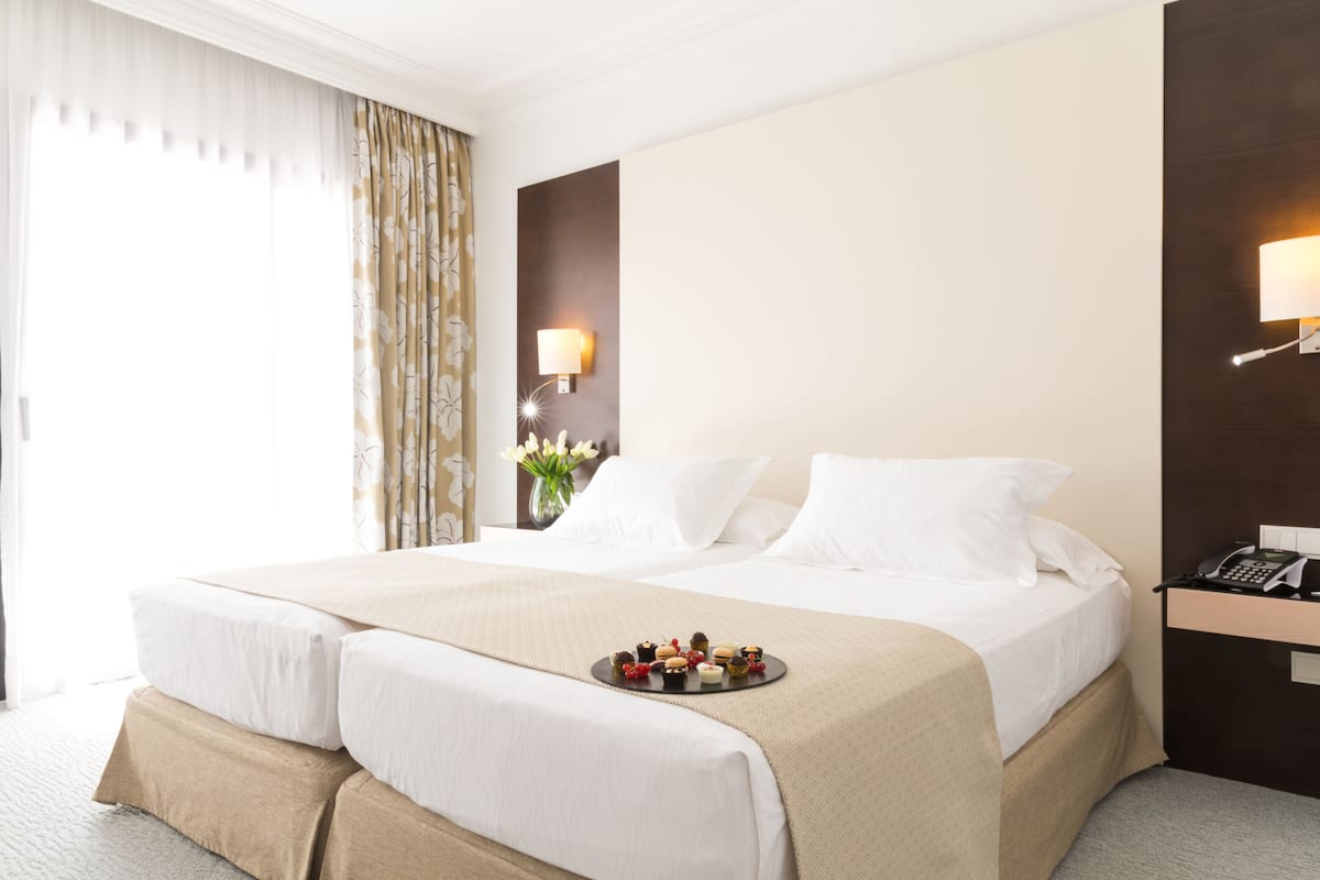 A hotel room with a large bed, a bedside table with a lamp, and a tray of snacks on the bed.