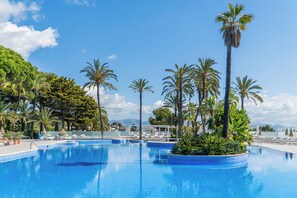 Una amplia piscina al aire libre rodeada de palmeras y sillones de descanso.