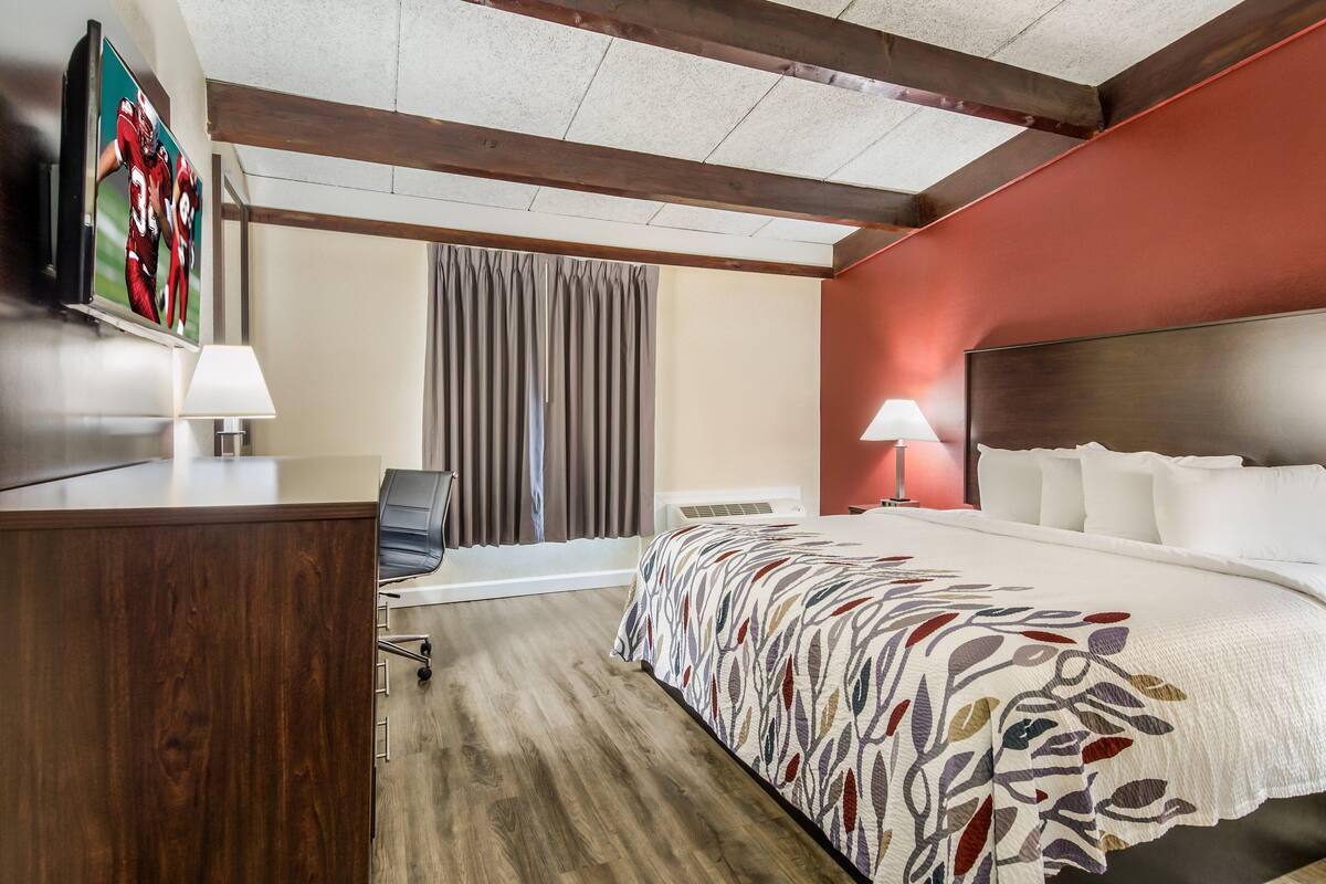 Une chambre d’hôtel avec un grand lit, un bureau avec une chaise, un téléviseur fixé au mur et une fenêtre avec des rideaux.