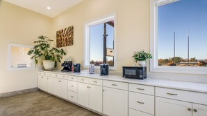 A kitchen with a long countertop, cabinets, a microwave, a coffee maker, and a potted plant. - Red Roof Inn Madison Heights, VA (Madison Heights)