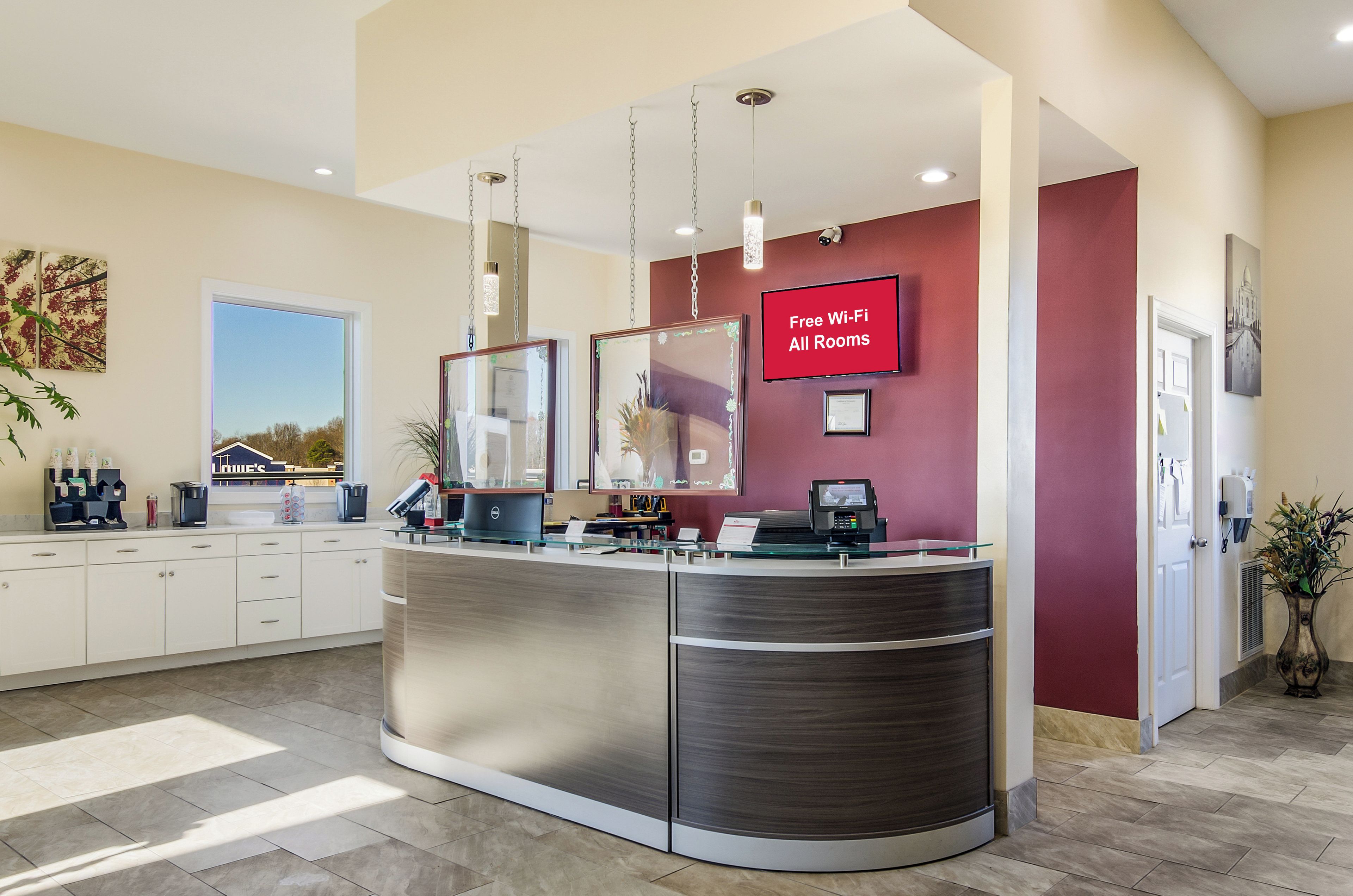 A reception area with a curved desk, a coffee machine, a computer, and a sign indicating free Wi-Fi in all rooms.