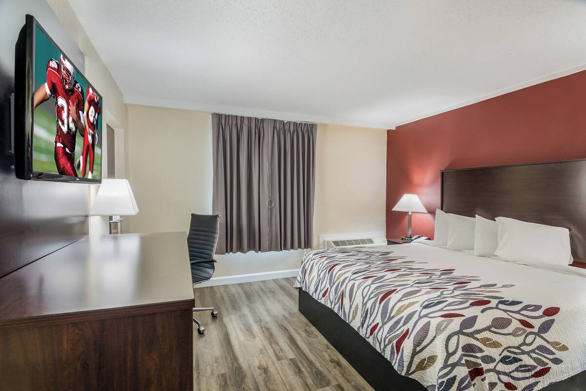 Une chambre d’hôtel avec un lit, un bureau, une chaise, une télévision et une fenêtre avec des rideaux.
