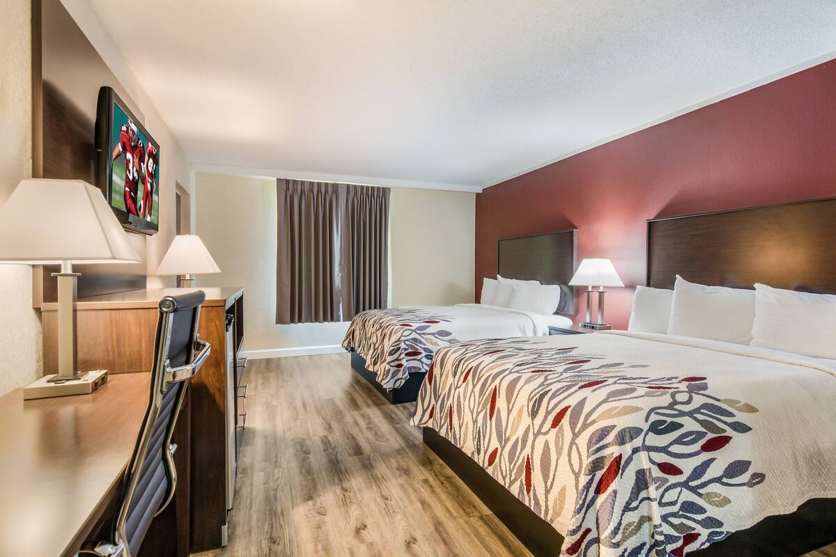Une chambre d’hôtel avec deux lits, un bureau, une chaise, une télévision et une fenêtre avec des rideaux.