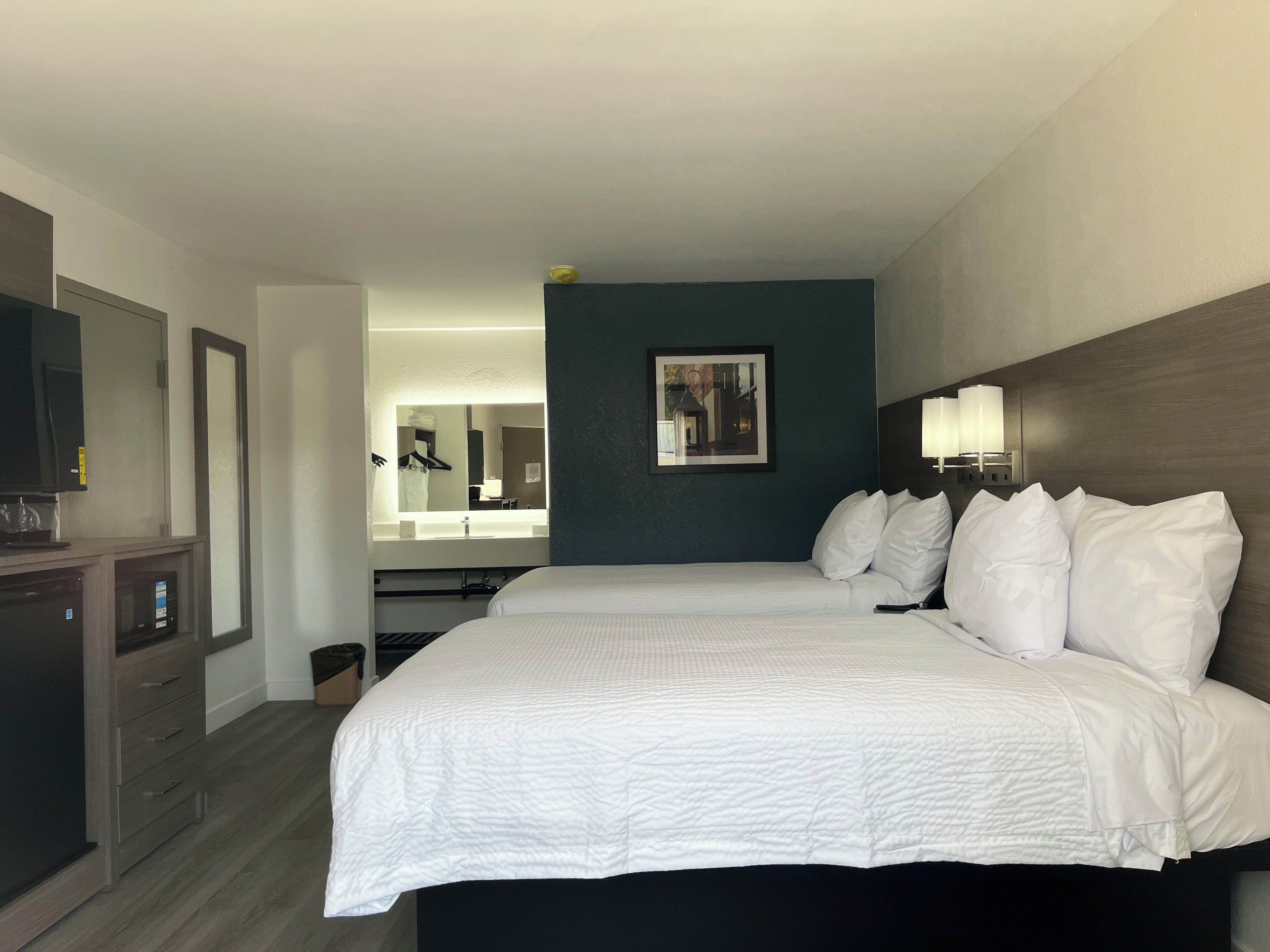 Une chambre d’hôtel équipée d’un lit, d’une télévision, d’un bureau avec un ordinateur, d’un miroir et d’un luminaire fixé au mur.