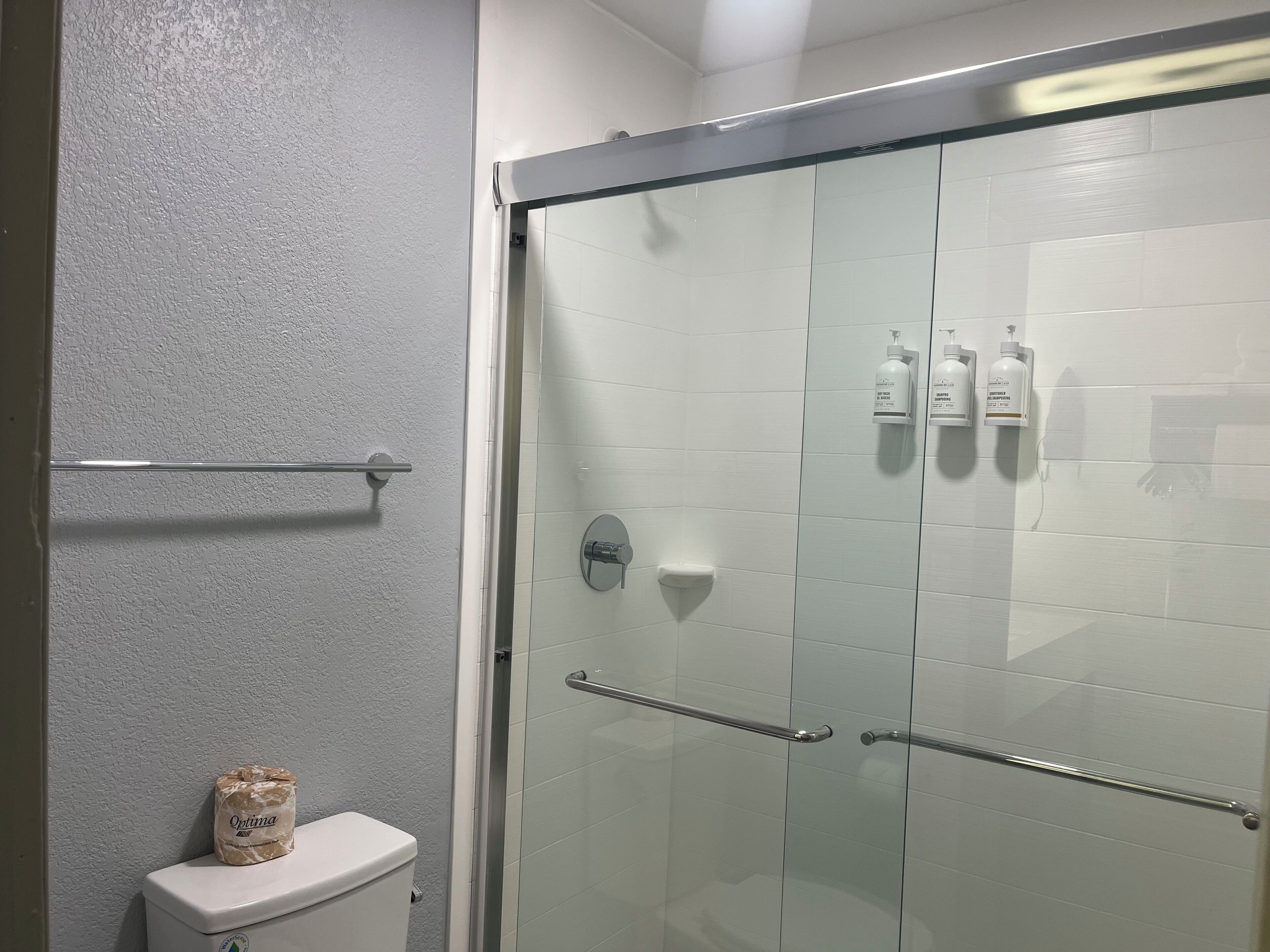 A bathroom with a glass shower enclosure, a toilet, and a towel rack.