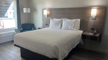 A hotel room with a large bed, bedside tables, a desk, a chair, a window with curtains, and wall-mounted lamps.
