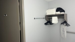 Casa de banho com porta-toalhas, toalha pendurada e prateleira com toalhas dobradas e um touca.