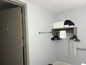 A bathroom with a towel rack, a hanging towel, and a shelf with folded towels and a cap.