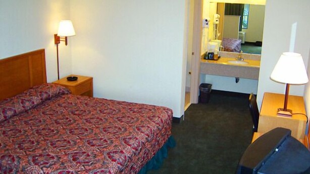 Quarto de hotel com cama, escrivaninha, cadeira, espelho e pia.