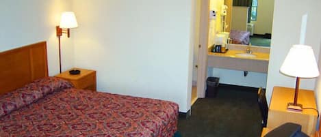A hotel room with a bed, a desk, a chair, a mirror, and a sink.
